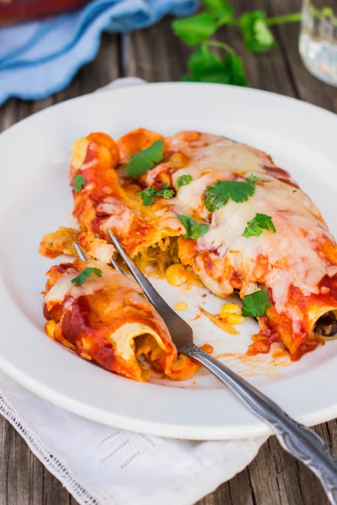 close up of spaghetti squash and black bean enchiladas on a plate with a fork