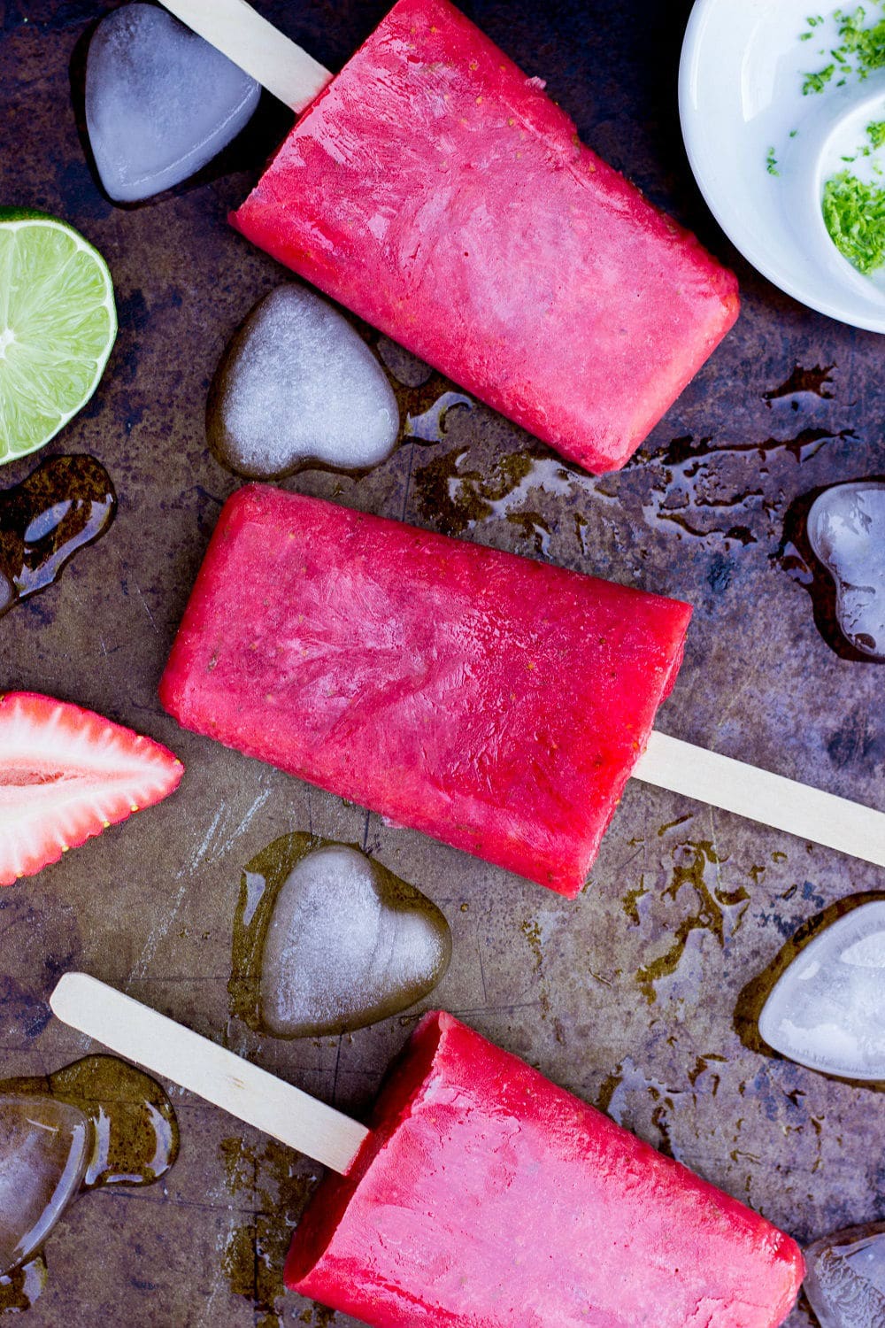 Strawberry Rhubarb & Lime Popsicles on a sheet pan with ice cubes