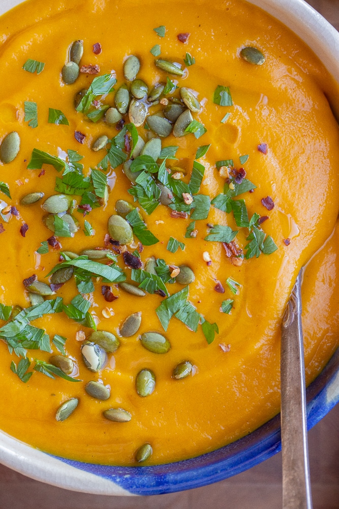 close up of roasted root vegetable soup in a bowl with pumpkin seeds and parsley
