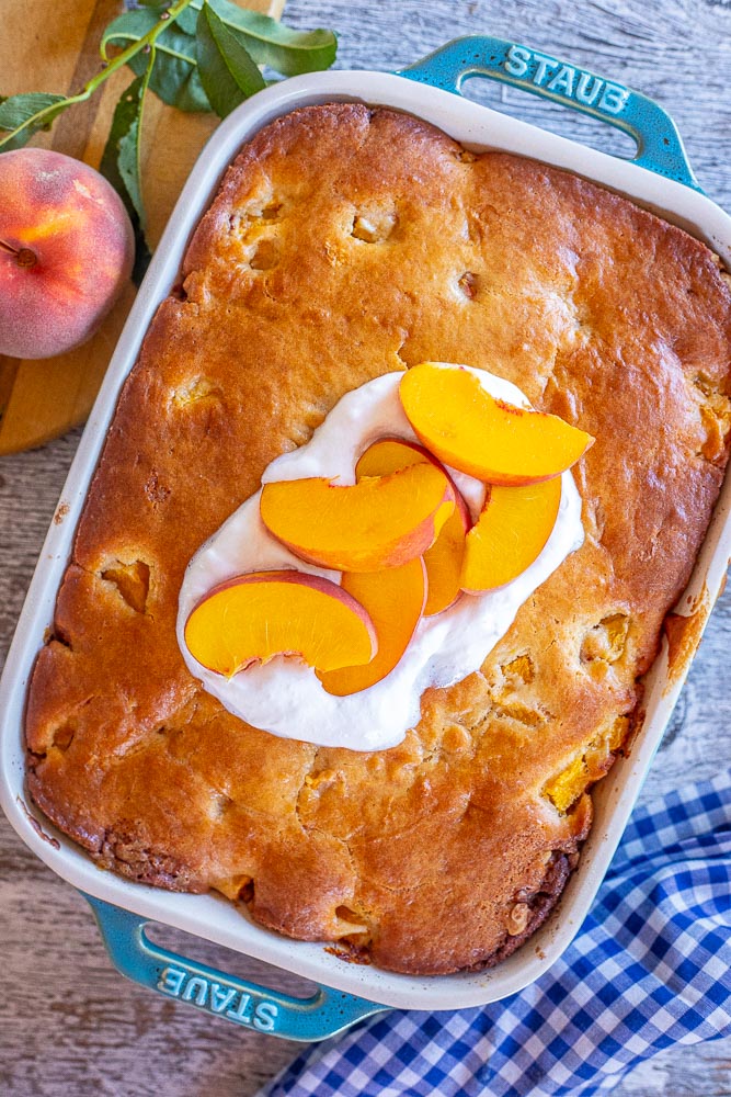Peach cake in a pan topped with peaches and whipped cream