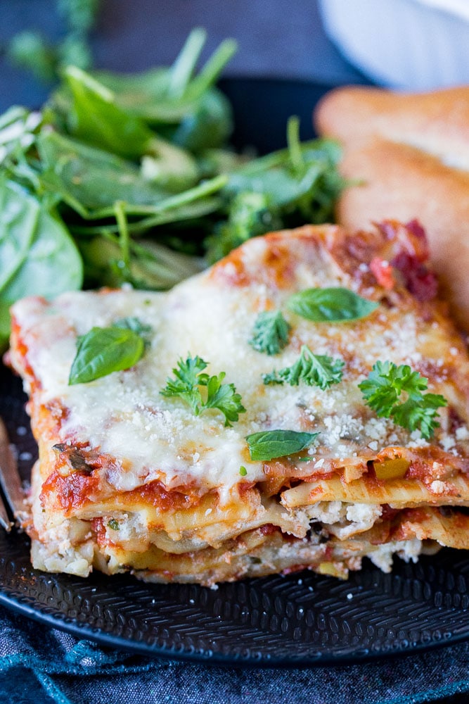 A big slice of vegetarian lasagna on a plate with salad and bread