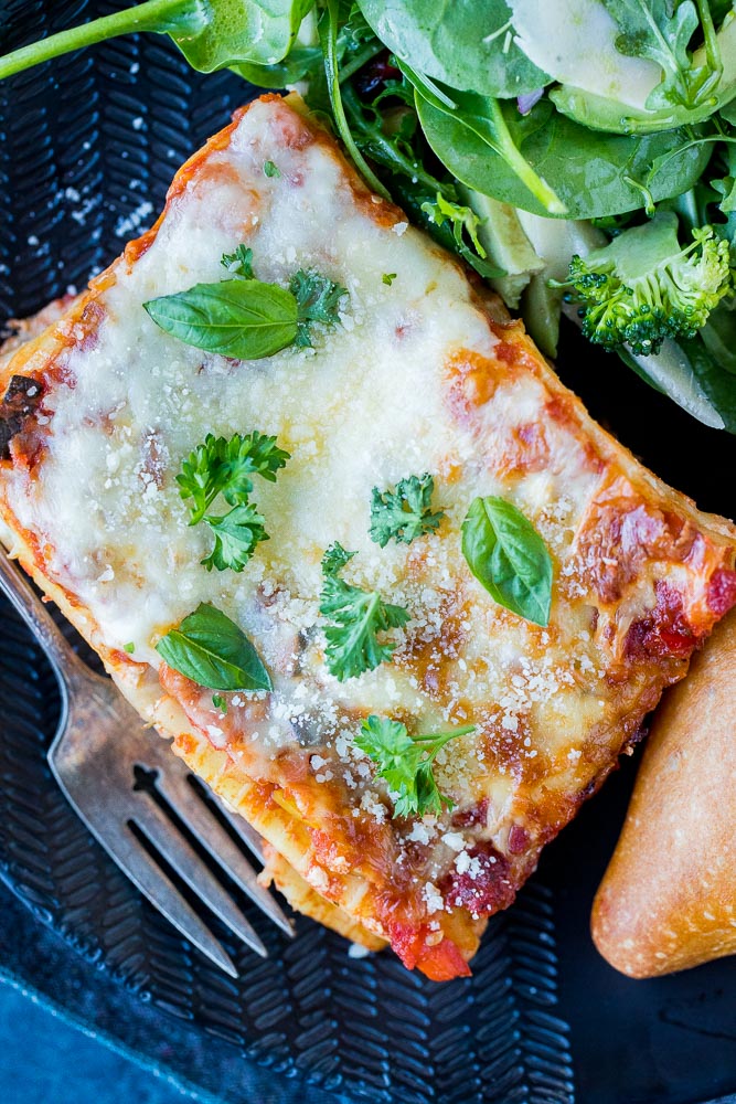 A big slice of vegetarian lasagna on a plate with salad