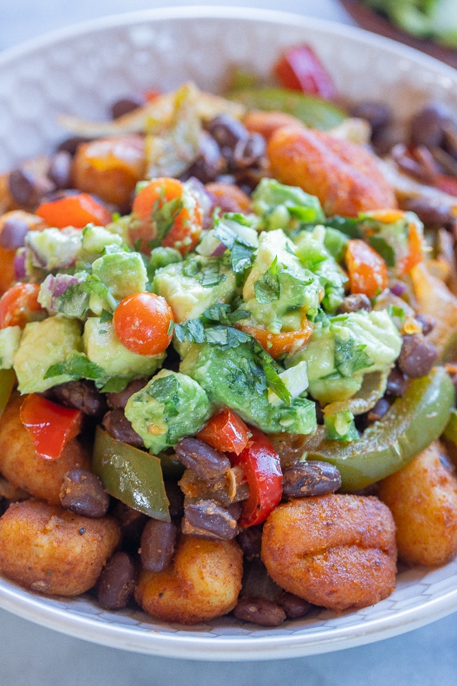 close up of a bowl of fajita gnocchi skillet with avocado salsa on top