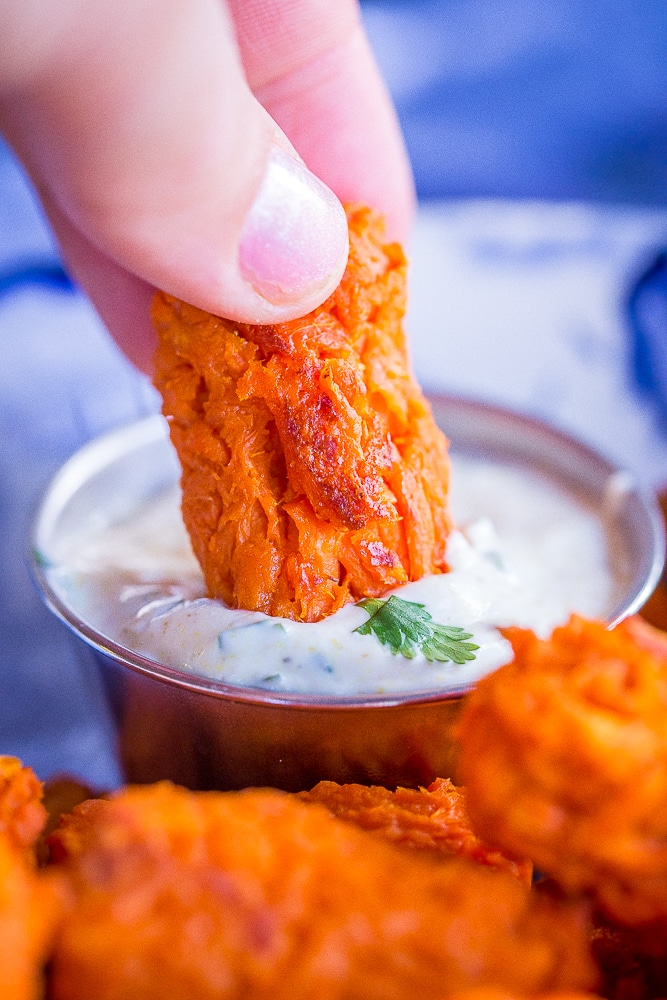 Close up of a sweet potato tot being dipped into curry cilantro dip.