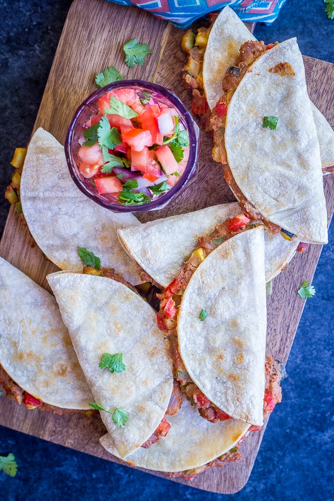 Crispy baked tacos with summer vegetables on a cutting board with a bowl of salsa