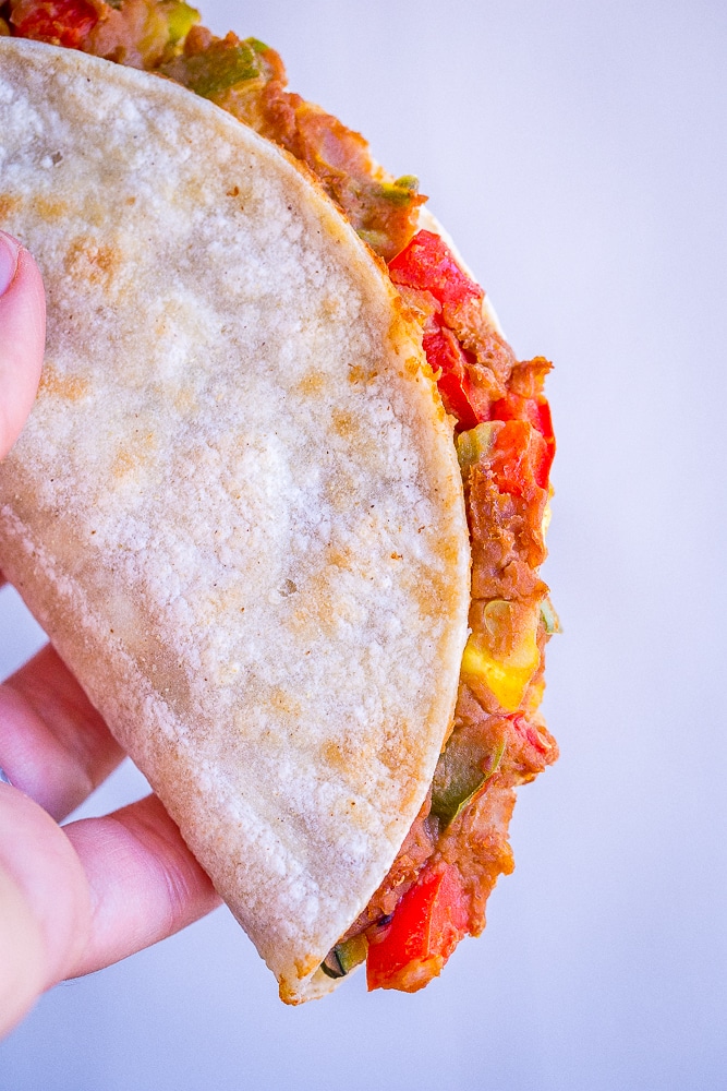 A crispy baked taco with summer vegetables being held in a hand so you can see the filling