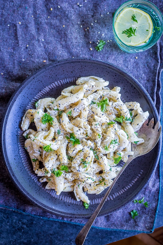 Overview of a plate of 30 Minute Creamy Goat Cheese Pasta with Everything Bagel Spice and a glass of water with a lemon in it.