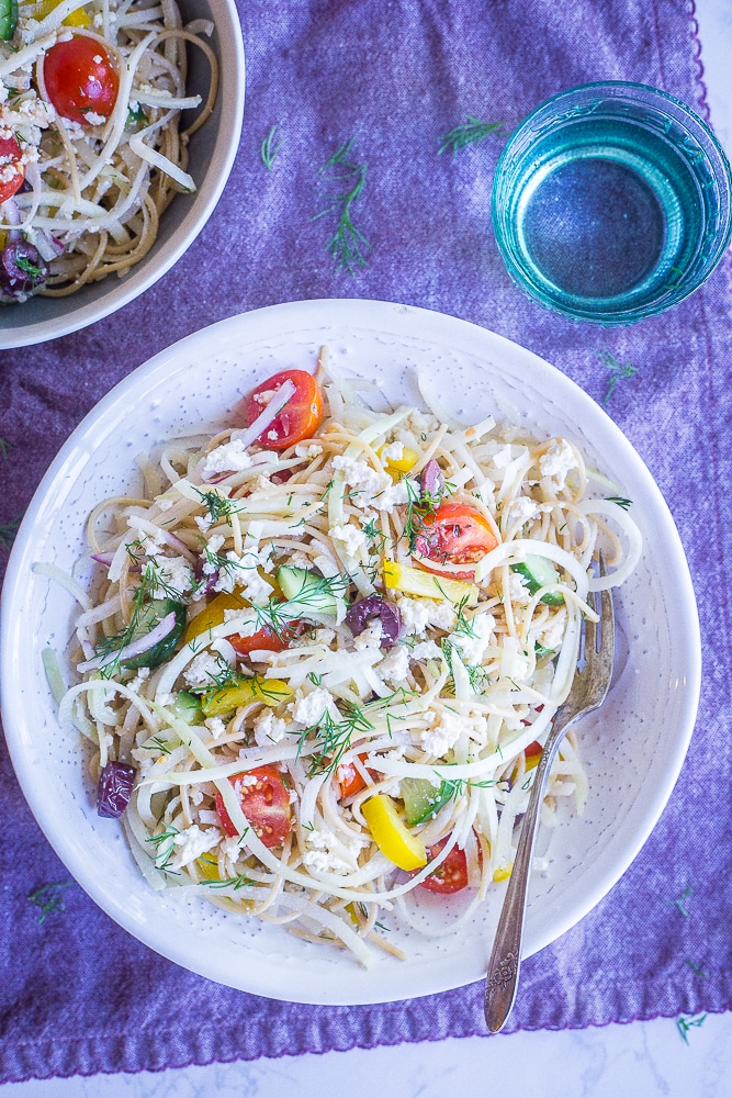Healthy Greek Pasta Salad with Kohlrabi Noodles in a white bowl on a purple napkin