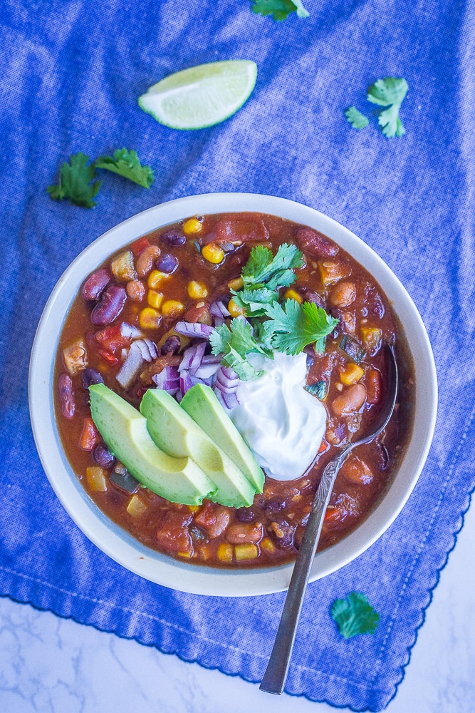 A bowl of instant pot vegetarian chili on a blue napkin with toppings