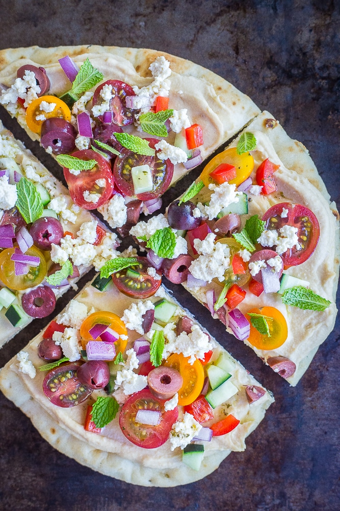 A No Cook Mediterranean Hummus Pita Pizza sliced into four slices