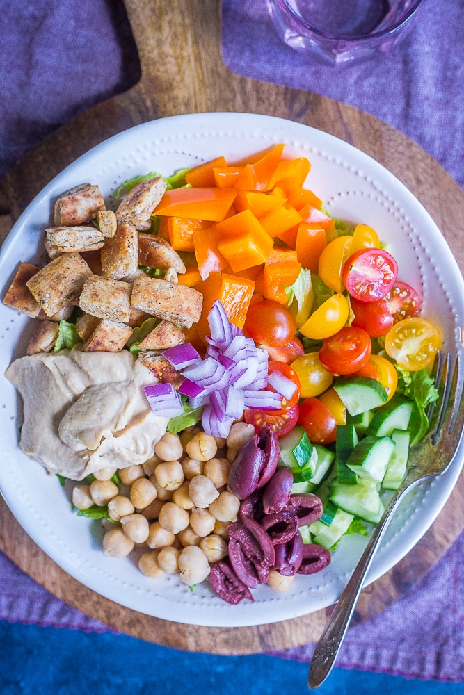 A big bowl of Easy Greek Salad Meal Prep Bowls on a cutting board with a purple napkin