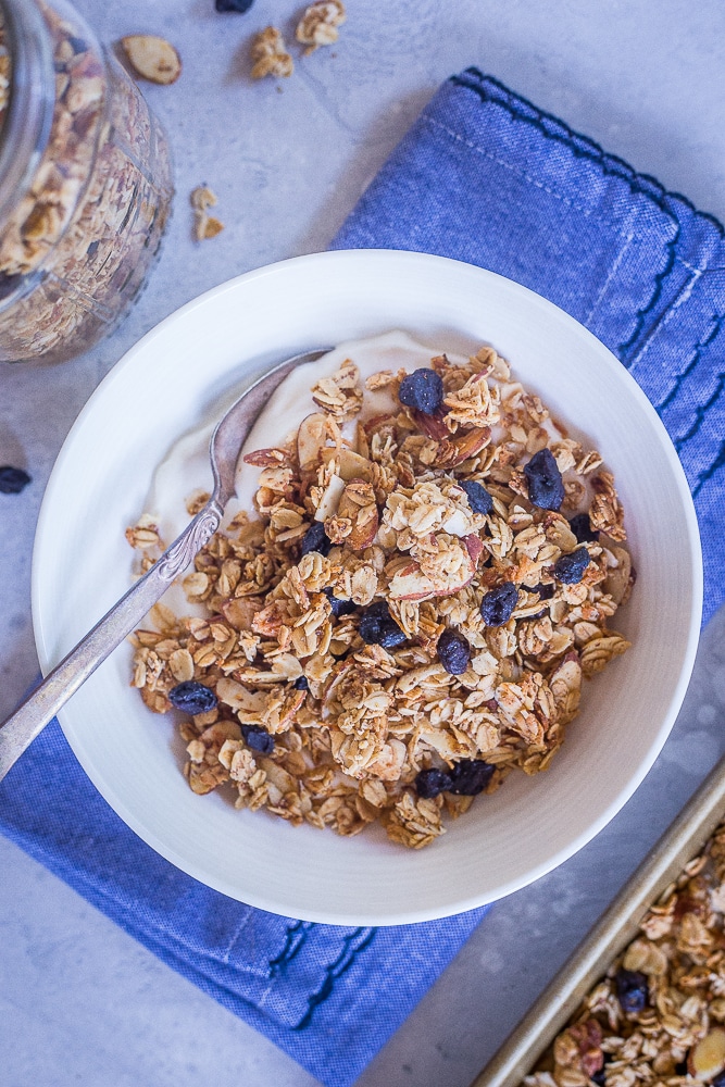 Bowl of Homemade Blueberry Almond Granola in a bowl with yogurt on a blue napkin.