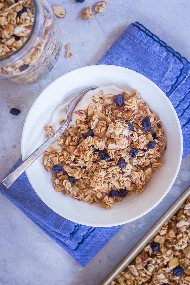 A bowl of Blueberry Almond Granola in a bowl with yogurt on a blue napkin