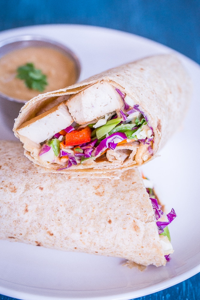 A Crunchy Asian Tofu Peanut Wraps cut in half on a plate with peanut sauce.