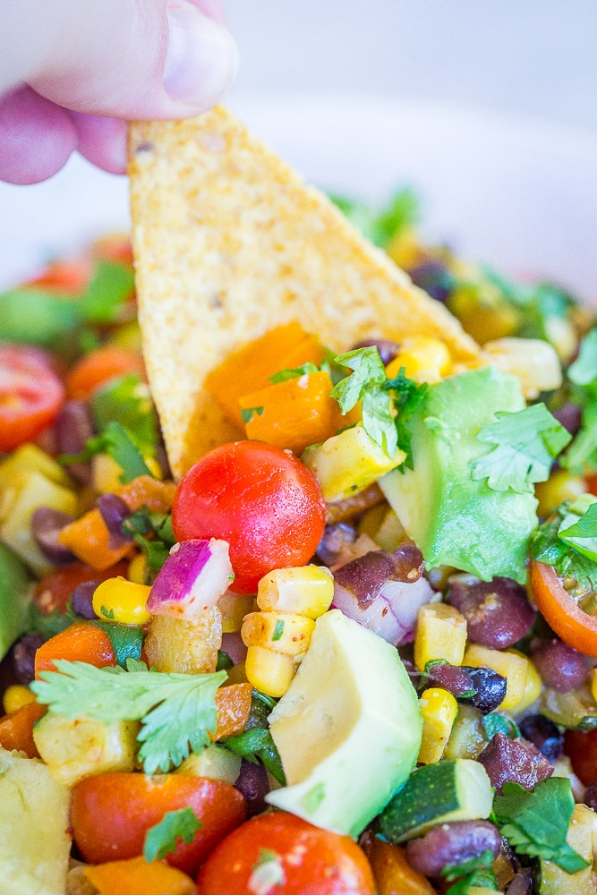 A bowl of Loaded Summer Vegetable Salad with Black Beans having a chip dipped into it.