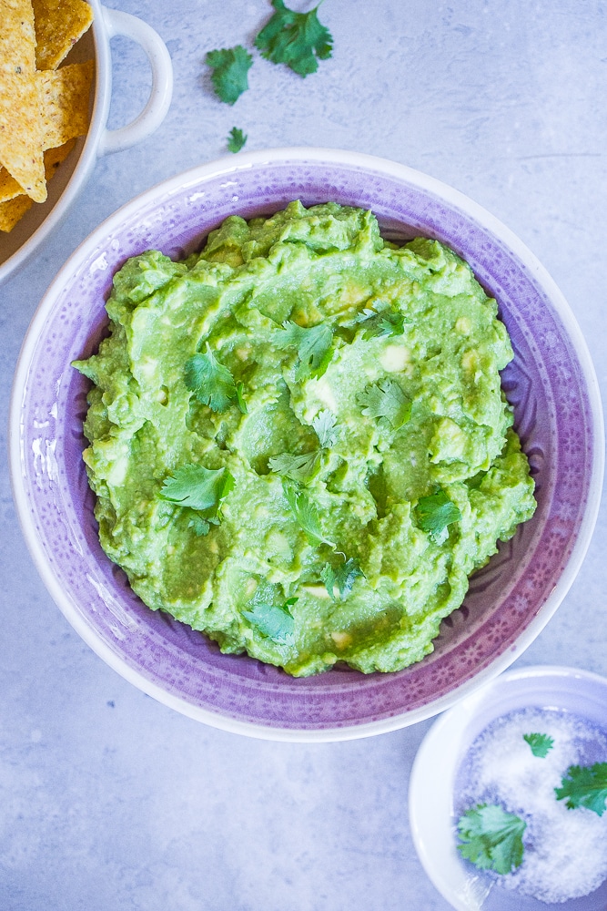 A bowl of The Best Easy Guacamole Recipe in a purple bowl with a side of chips