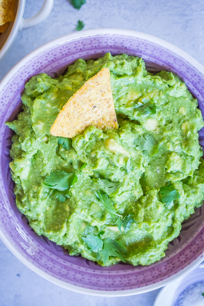 A bowl of The Best Easy Guacamole in a purple bowl with a chip in it.