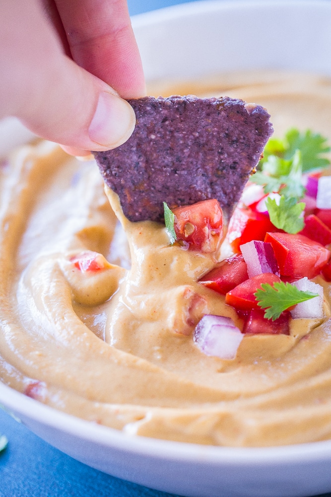 A chip dipping into a bowl of Creamy Cauliflower Queso Dip
