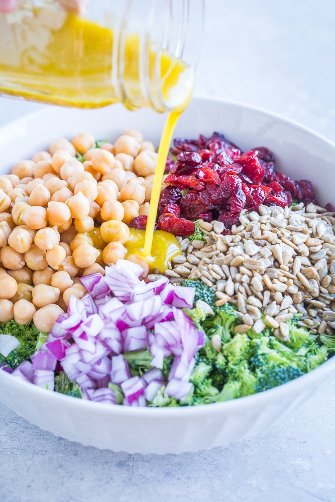 Bowl of Crunchy Broccoli Salad with Maple Mustard Dressing being poured over it