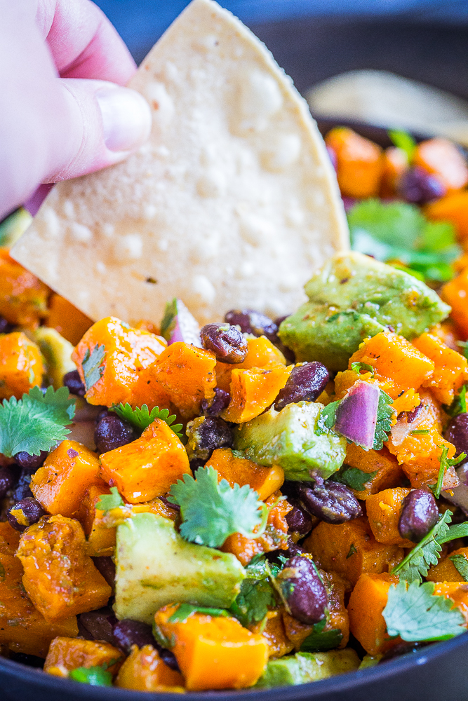 A hand dipping a chip into a bowl of Roasted Butternut Squash Salad with Black Beans