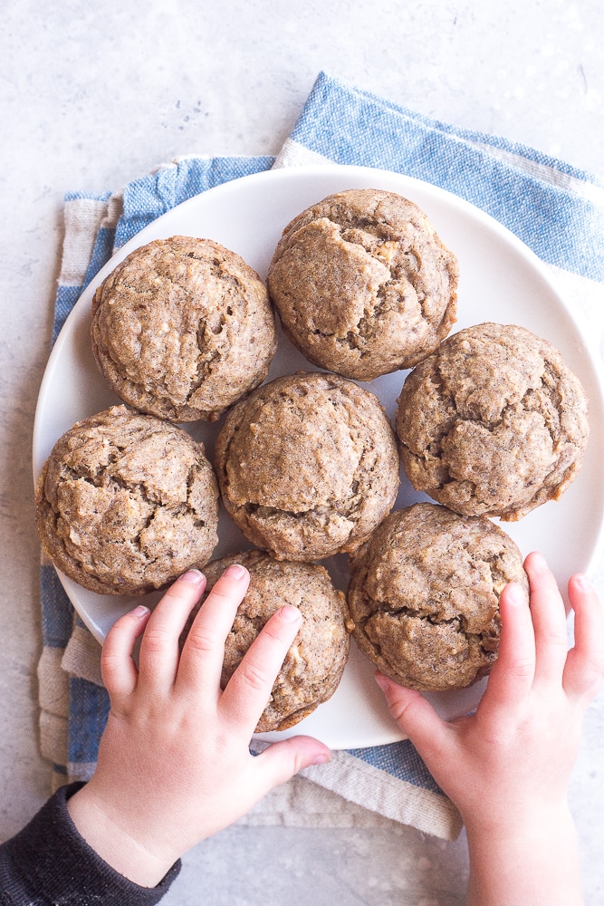 Toddler hands grabbing these Healthy Banana Muffins from a plate