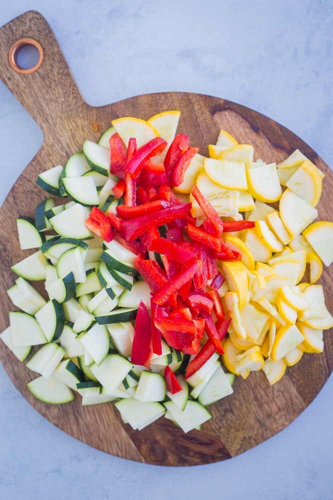 Summer vegetables cut up on a cutting board for pesto pasta with summer vegetables recipe