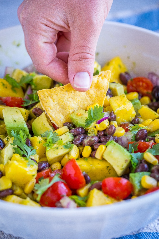 Hand dipping a chip in black bean salad with mango and avocado