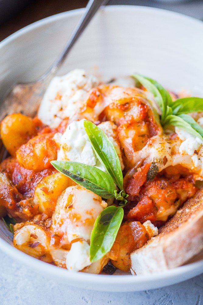 Close up of gnocchi lasagna bake in a bowl with basil and bread