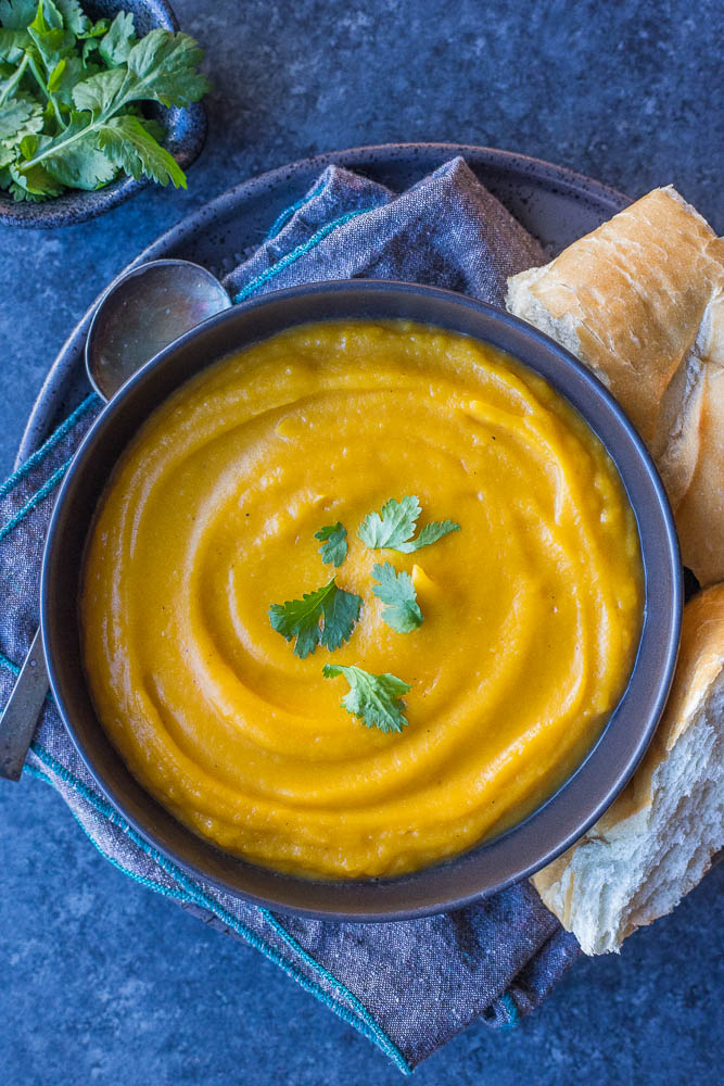 Bowl of butternut squash soup on a plate with some bread and cilantro leaves