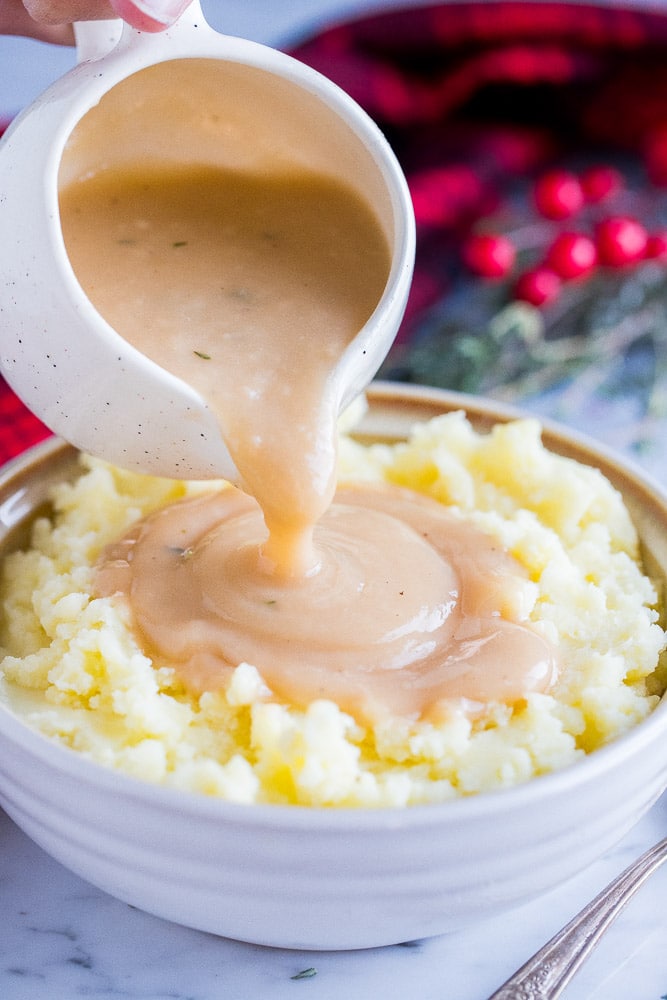 easy vegan gravy in a saucer cup being poured over a bowl of mashed potatoes