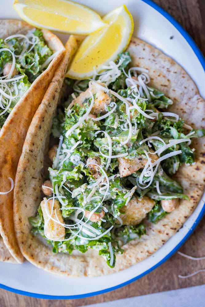 Close up of a kale Caesar salad pita on a plate with lemon wedges
