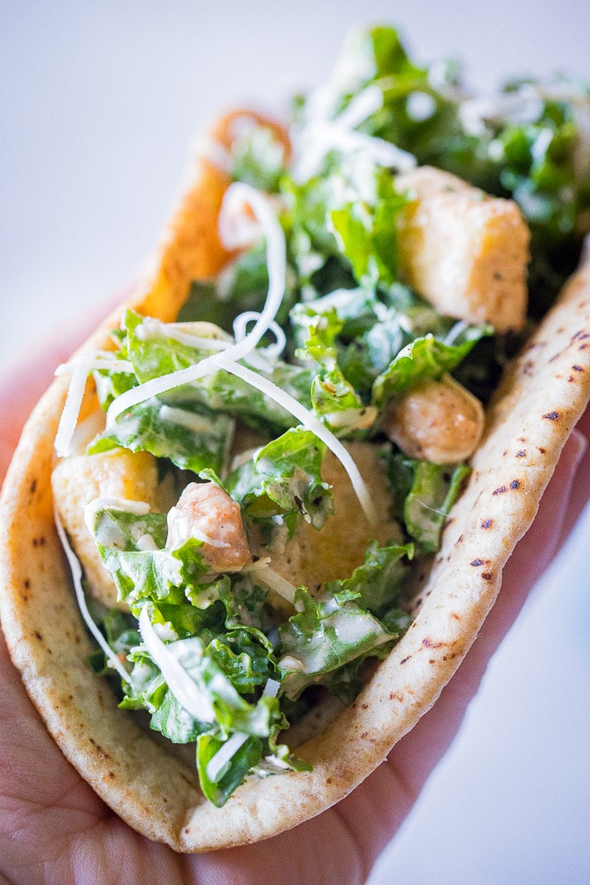 Close up of a hand holding a kale Caesar salad pita