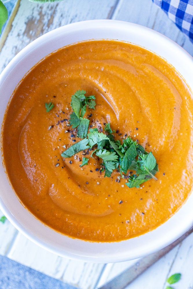 Close up of a bowl of tomato soup with fresh herbs