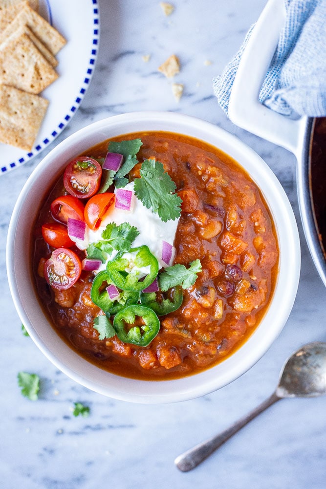 Flatlay photo of a bowl of vegetarian chili with crackers and toppings