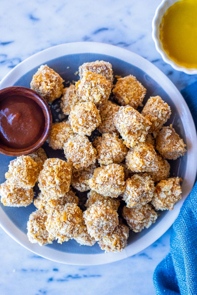 A plate full of crispy tofu nuggets with ketchup and honey mustard