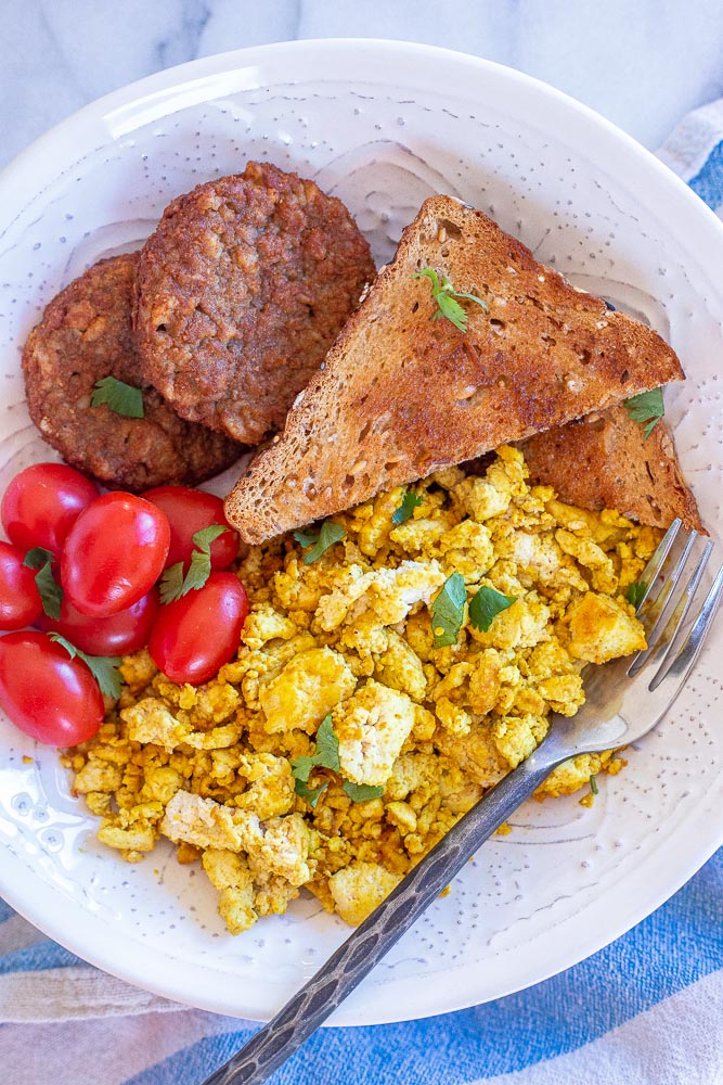 tofu scramble in a bowl with toast, tomatoes and veggie sausage