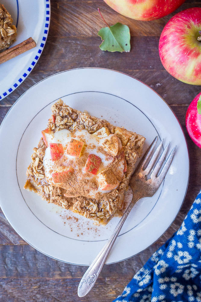 a slice of apple cinnamon baked oatmeal on a plate with yogurt and apples