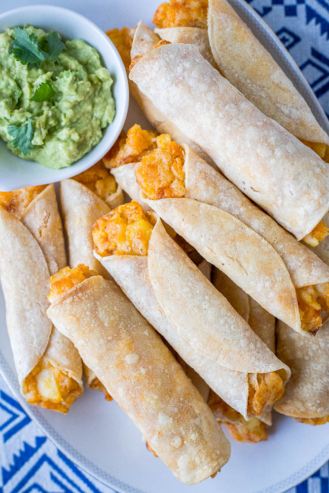 plate of cheesy potato taquitos with a bowl of guacamole