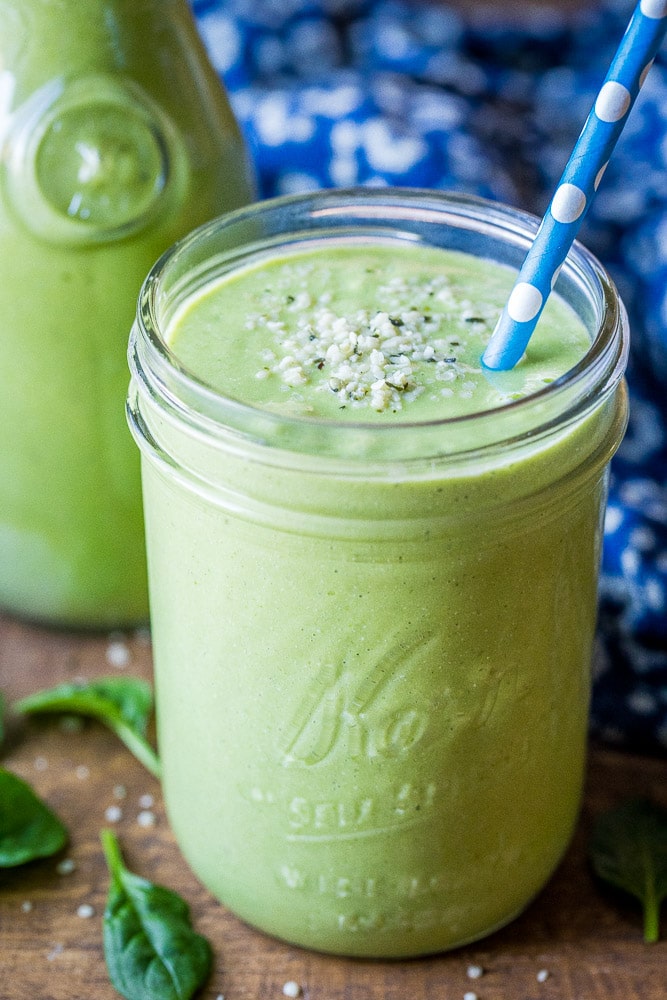 a green smoothie in a glass cup with a blue straw