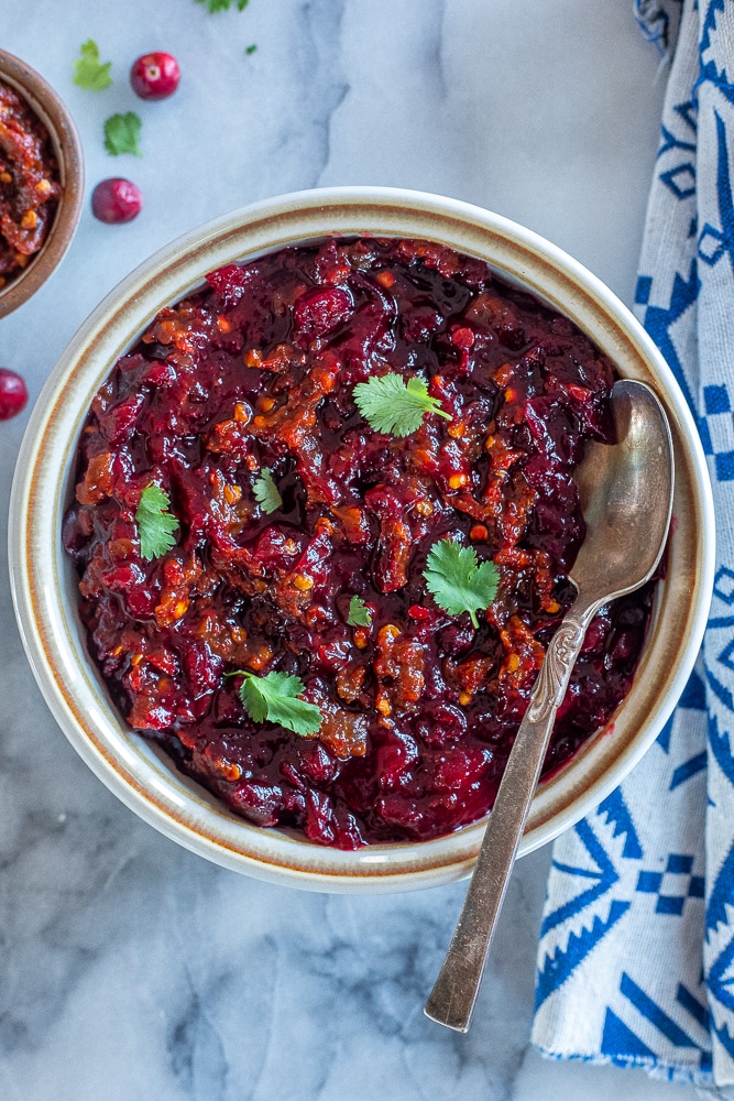 a bowl of chipotle cranberry sauce in a bowl with a spoon and cilantro leaves as a garnish