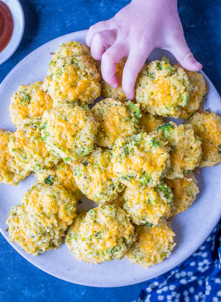 A plate of broccoli rice casserole bites with a child's hand taking one