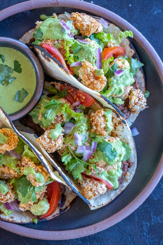 a plate with three crispy cauliflower tacos and a bowl of green tahini sauce