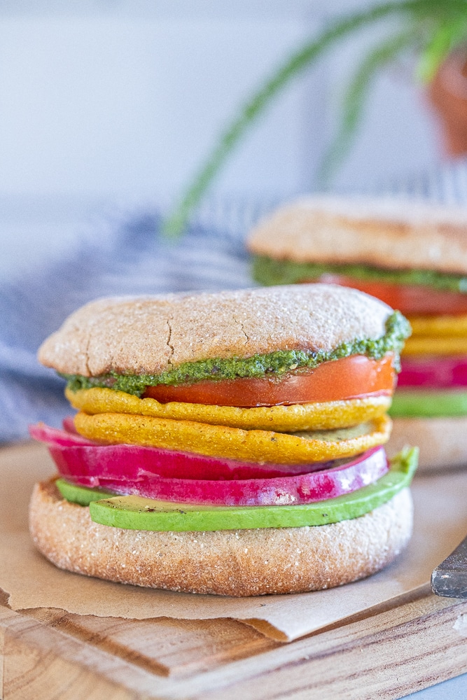 close up of a vegan breakfast sandwich with avocado, onion, tomato and pesto on an English muffin