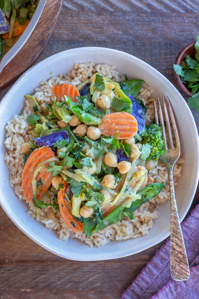 a bowl of Thai green curry with chickpeas and vegetables over brown rice