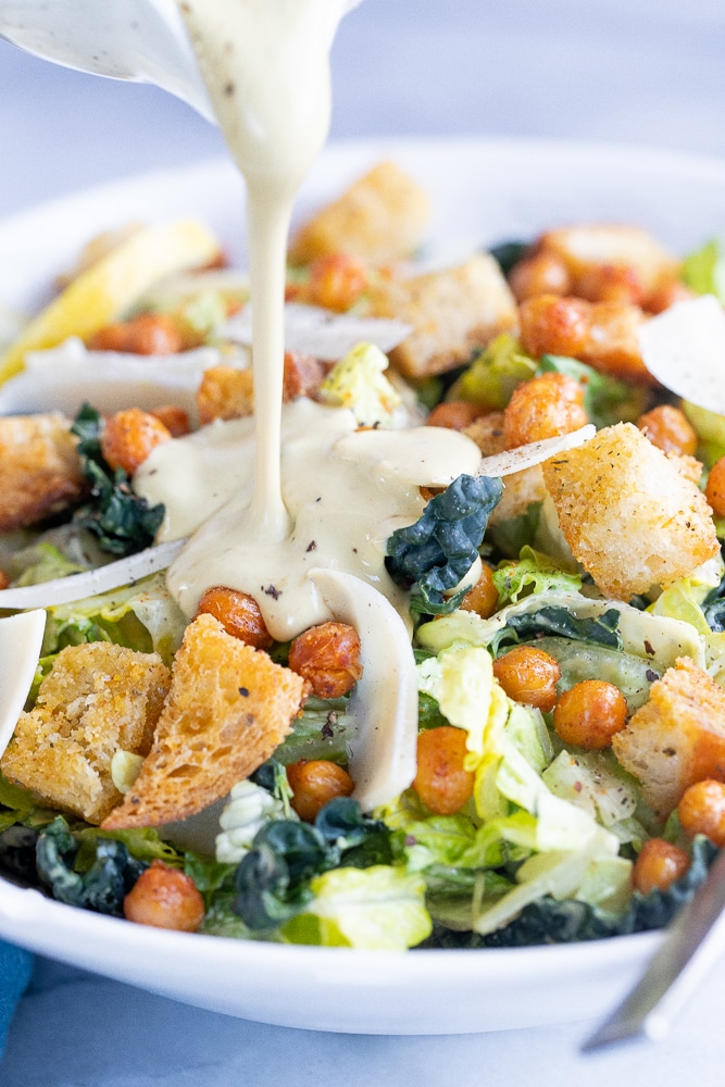 vegan caesar dressing being poured on a Caesar salad