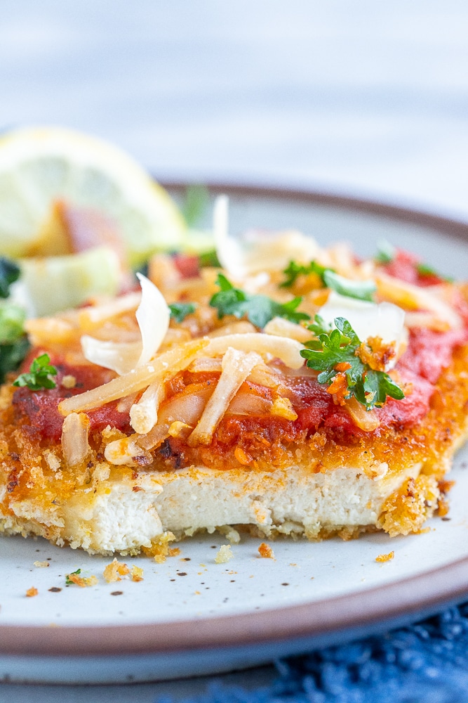 a slice of tofu parmesan with a bite taken out of it