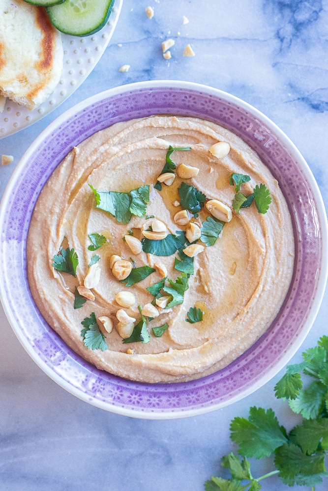 a bowl of peanut butter hummus garnished with toasted sesame oil, roasted peanuts and cilantro