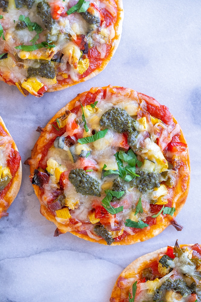 mini tortilla pizzas with roasted veggies on a cutting board