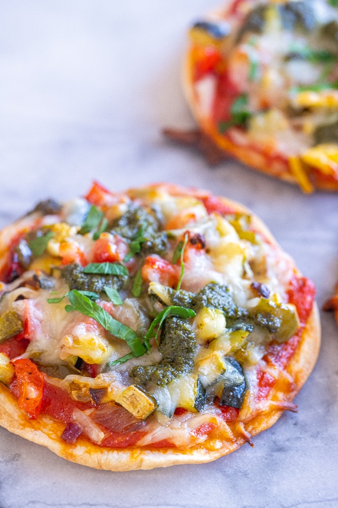 close up of a tortilla pizza with roasted vegetables and pesto