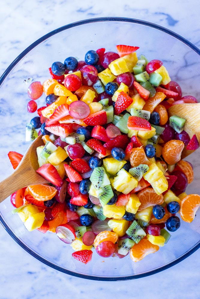 rainbow fruit salad all mixed together in a bowl with wooden spoons